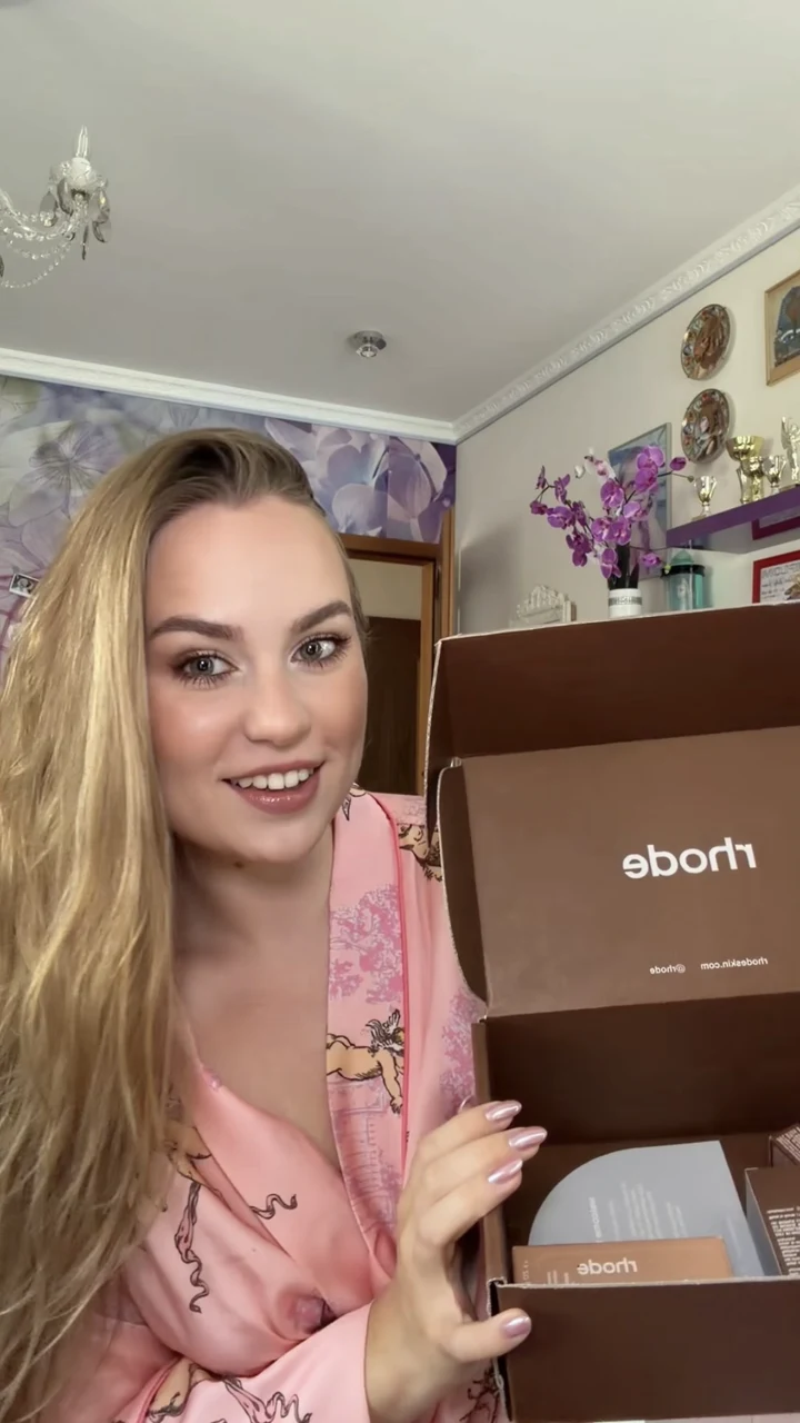 Sofiya holding an open Rhode makeup package while wearing a pink robe